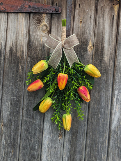 Artificial yellow and orange tulip door swag with tealeaf foliage finished with a hessian bow.