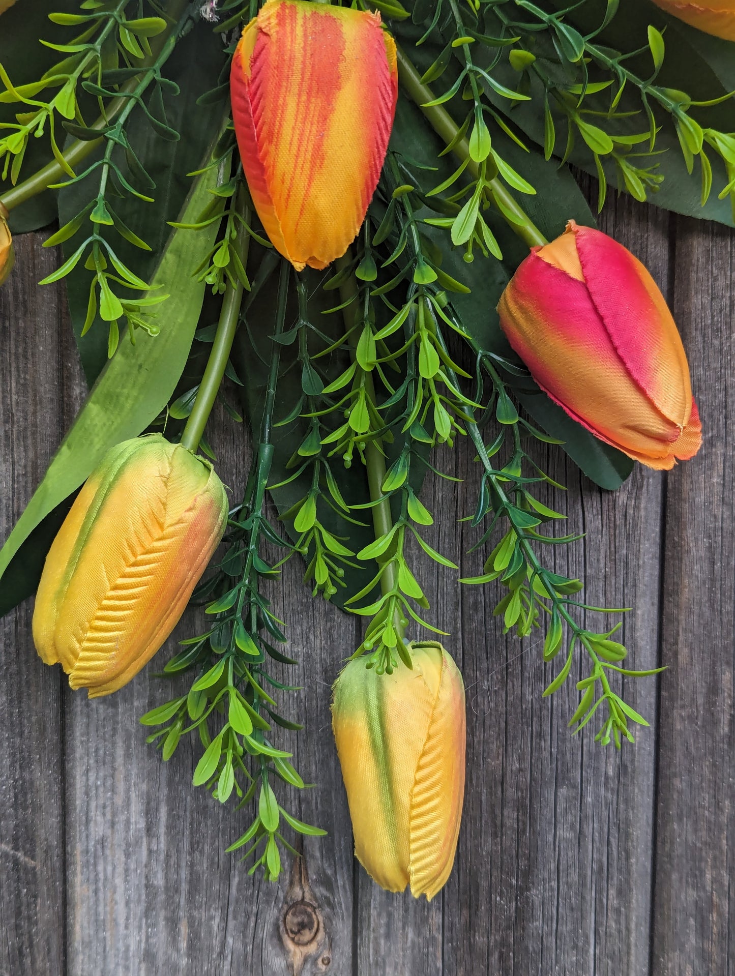 Artificial yellow and orange tulip door swag with tealeaf foliage finished with a hessian bow.