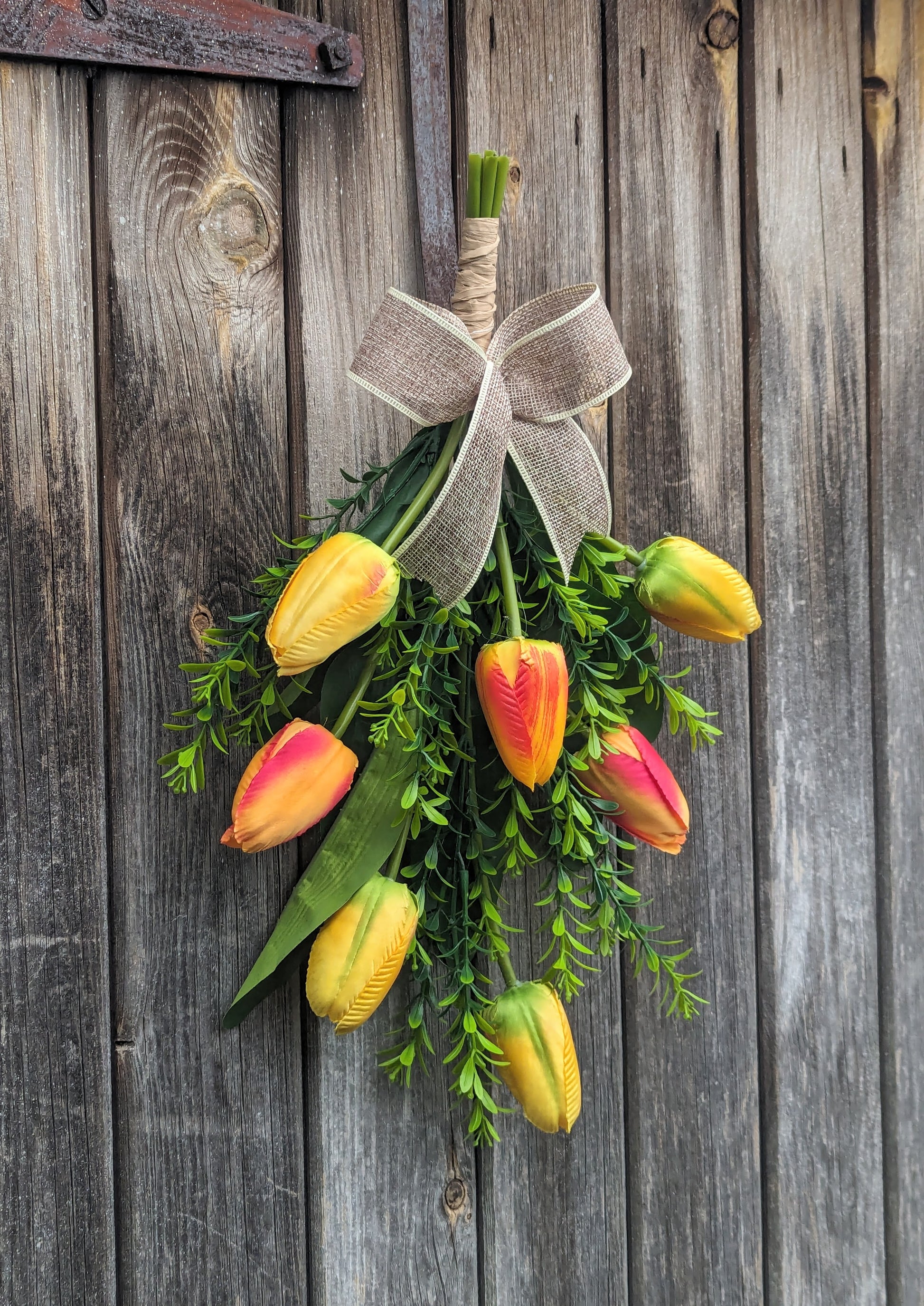 Artificial yellow and orange tulip door swag with tealeaf foliage finished with a hessian bow.