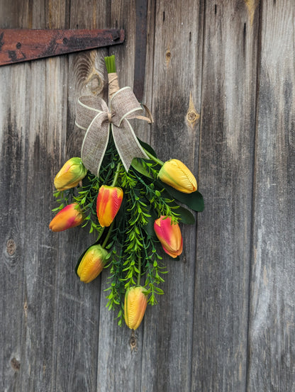 Artificial yellow and orange tulip door swag with tealeaf foliage finished with a hessian bow.