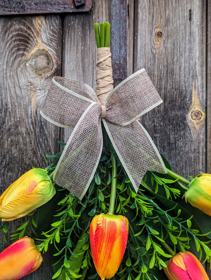 Artificial yellow and orange tulip door swag with tealeaf foliage finished with a hessian bow.